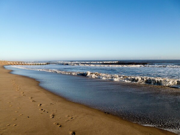 A beach with footprints, waves, and a clear sky.