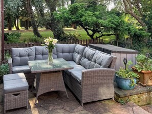 A wicker sectional sofa with a glass-top table, a small ottoman, and a potted plant.