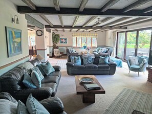A spacious living area with leather sofas, a wooden coffee table, and large windows offering a view of the outdoors.