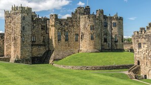 A historic castle with multiple towers and a flagpole. - 2 bedroom accommodation in Embleton, near Alnwick (Embleton, near Alnwick)
