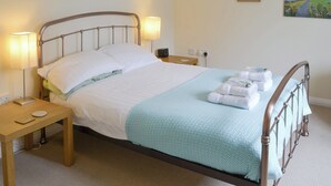 A neatly made bed with a metal frame, two bedside tables with lamps, and artwork on the walls. - 2 bedroom accommodation in Embleton, near Alnwick (Embleton, near Alnwick)