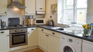 A kitchen with white cabinets, a stove, a microwave, a toaster, and a washing machine. - 2 bedroom accommodation in Embleton, near Alnwick (Embleton, near Alnwick)