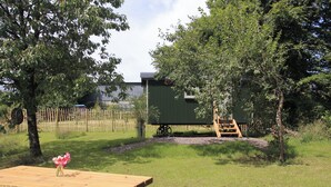 A wooden picnic table with a vase of flowers, surrounded by a grassy area with trees and a green building in the background. - 1 bedroom accommodation in Dippertown, near Tavistock (Dippertown, near Tavistock)