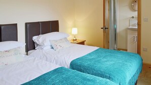 Ein Hotelzimmer mit zwei Betten, einem Nachttisch mit Lampe, einem Badezimmer mit Spiegel und Waschbecken sowie einer Holztür.