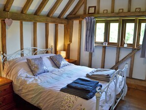 A bedroom with a bed, a nightstand, a window with curtains, and wooden beams on the ceiling.
