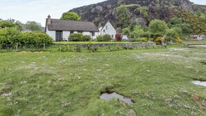 Een wit huis met een pannendak, omgeven door een grasveld en een stenen muur.