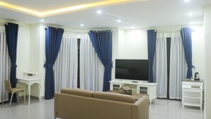 A modern living room with a flat-screen TV, a sofa, a desk, and curtains. - QB Casa Residence (Dong Hoi)
