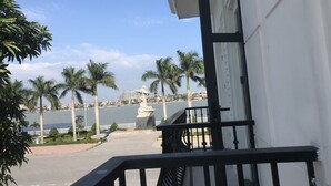 A balcony with a view of a waterfront, palm trees, and a statue. - QB Casa Residence (Dong Hoi)