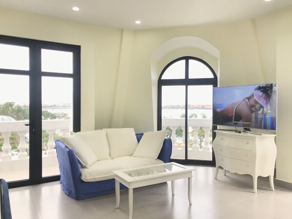 A modern living room with a white sofa, a coffee table, a TV, and a balcony with a view. - QB Casa Residence (Dong Hoi)