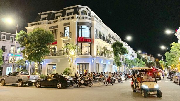 A multi-story building with a restaurant on the ground floor, multiple balconies, and a parking area with cars and motorcycles. - QB Casa Residence (Dong Hoi)