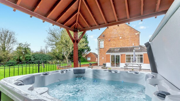 A hot tub under a wooden pergola with a brick house in the background. - 4 bedroom accommodation in West Huntspill, Highbridge (West Huntspill, Highbridge)