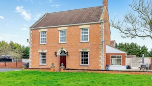 A two-story brick house with a red door, multiple windows, and a small attached garage. - 4 bedroom accommodation in West Huntspill, Highbridge (West Huntspill, Highbridge)