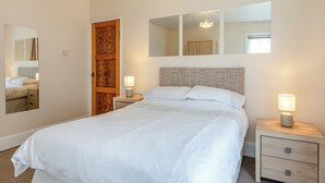 A bedroom with a bed, two bedside tables, a wooden door, and a mirror. - 4 bedroom accommodation in West Huntspill, Highbridge (West Huntspill, Highbridge)