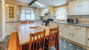 A kitchen with white cabinets, a wooden dining table, and a tiled floor. - 4 bedroom accommodation in West Huntspill, Highbridge (West Huntspill, Highbridge)