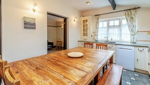 A kitchen with a wooden table, chairs, a dishwasher, and a window with curtains. - 4 bedroom accommodation in West Huntspill, Highbridge (West Huntspill, Highbridge)