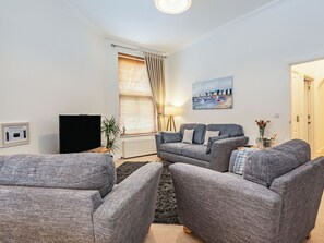 Ett vardagsrum med en grå soffgrupp, en platt-TV och en tavla som föreställer ett kustlandskap.