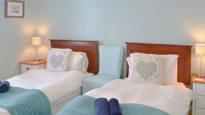 Ein Hotelzimmer mit zwei Einzelbetten, jeweils mit Holz-Kopfteilen, weißer Bettwäsche und dekorativen Kissen. Zwei Nachttische mit Lampen und ein gerahmtes Bild an der Wand sind ebenfalls vorhanden.