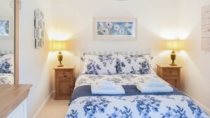 Ein Schlafzimmer mit einem Bett, zwei Nachttischen mit Lampen, einer Pendelleuchte, einem gerahmten Bild an der Wand und einem Spiegel links.