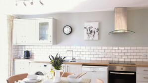 Eine moderne Küche mit weißen Schränken, einem Geschirrspüler, einem Backofen und einem Essbereich mit Tisch und Stühlen.