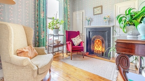 Una sala de estar acogedora con chimenea, papel tapiz floral y un sillón rojo.