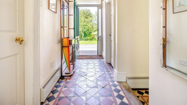 Un pasillo con baldosas estampadas, una puerta con picaporte de latón y vistas a zonas verdes.