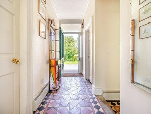 Un couloir avec des carreaux de sol à motifs, une porte dotée d’une poignée en laiton et une vue sur la verdure à l’extérieur.