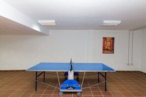 Une pièce avec une table de ping-pong bleue, des murs blancs et une affiche accrochée au mur.