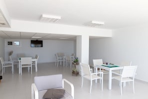 Una sala riunioni ampia e luminosa, con arredi bianchi, una televisione a schermo piatto e luci a soffitto.