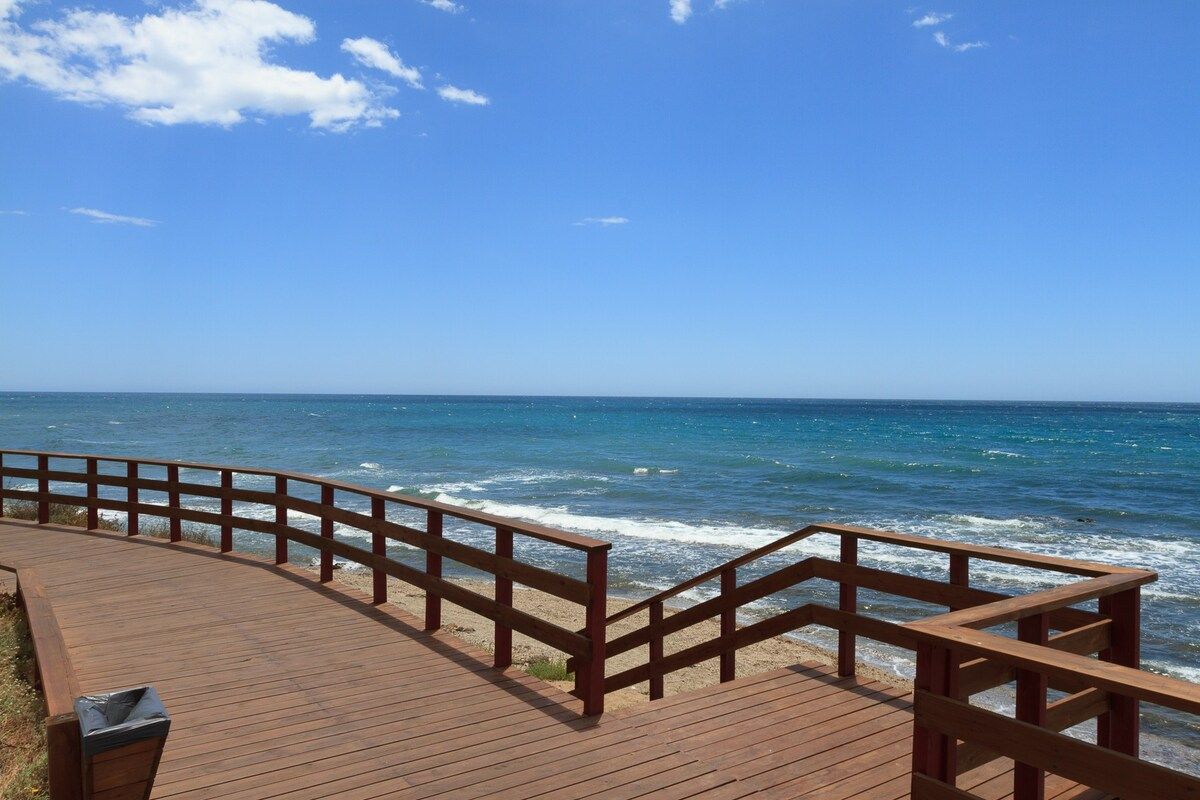 A wooden boardwalk leading to the ocean with a clear sky.