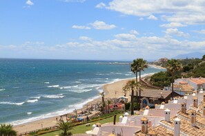 Un hôtel situé sur la côte, avec vue sur la plage, comprenant plusieurs chambres dotées de balcons et un espace piscine.