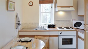 Cocina compacta con lavamanos, estufa, microondas y comedor con mesa para dos.