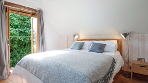 Ett sovrum med en stor säng, en sänggavel i trä, sänglampor och utsikt över grönskan genom ett fönster.
