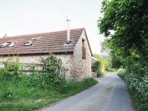 A rural road leading to a stone building with a tiled roof and a chimney.