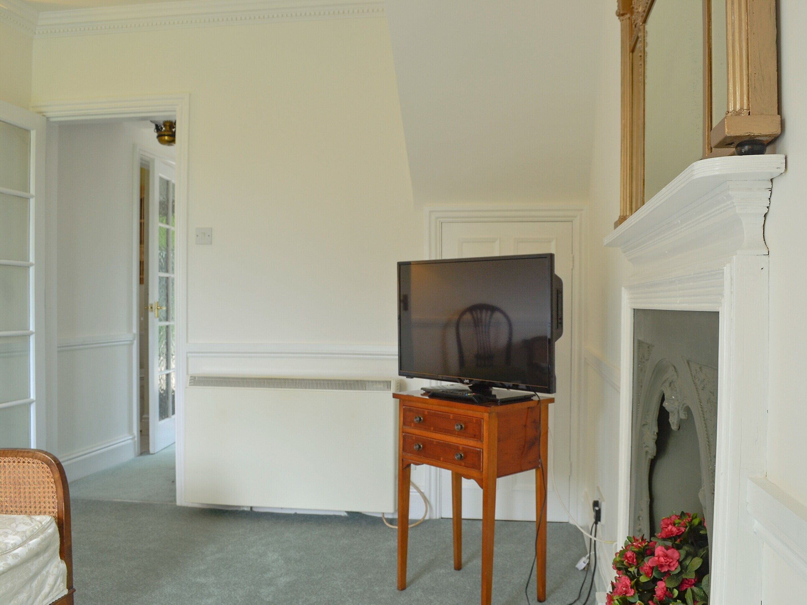 A room with a television on a wooden stand, a fireplace, and a door leading to another room.