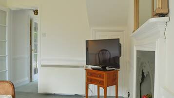 A room with a television on a wooden stand, a fireplace, and a door leading to another room.