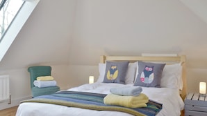 Un letto ben rifatto con cuscini e coperta, una sedia con asciugamani e vista sul cielo attraverso una finestra.
