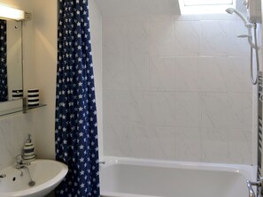 A bathroom with a white sink, a mirror, a shower with a handheld showerhead, and a window above the shower.