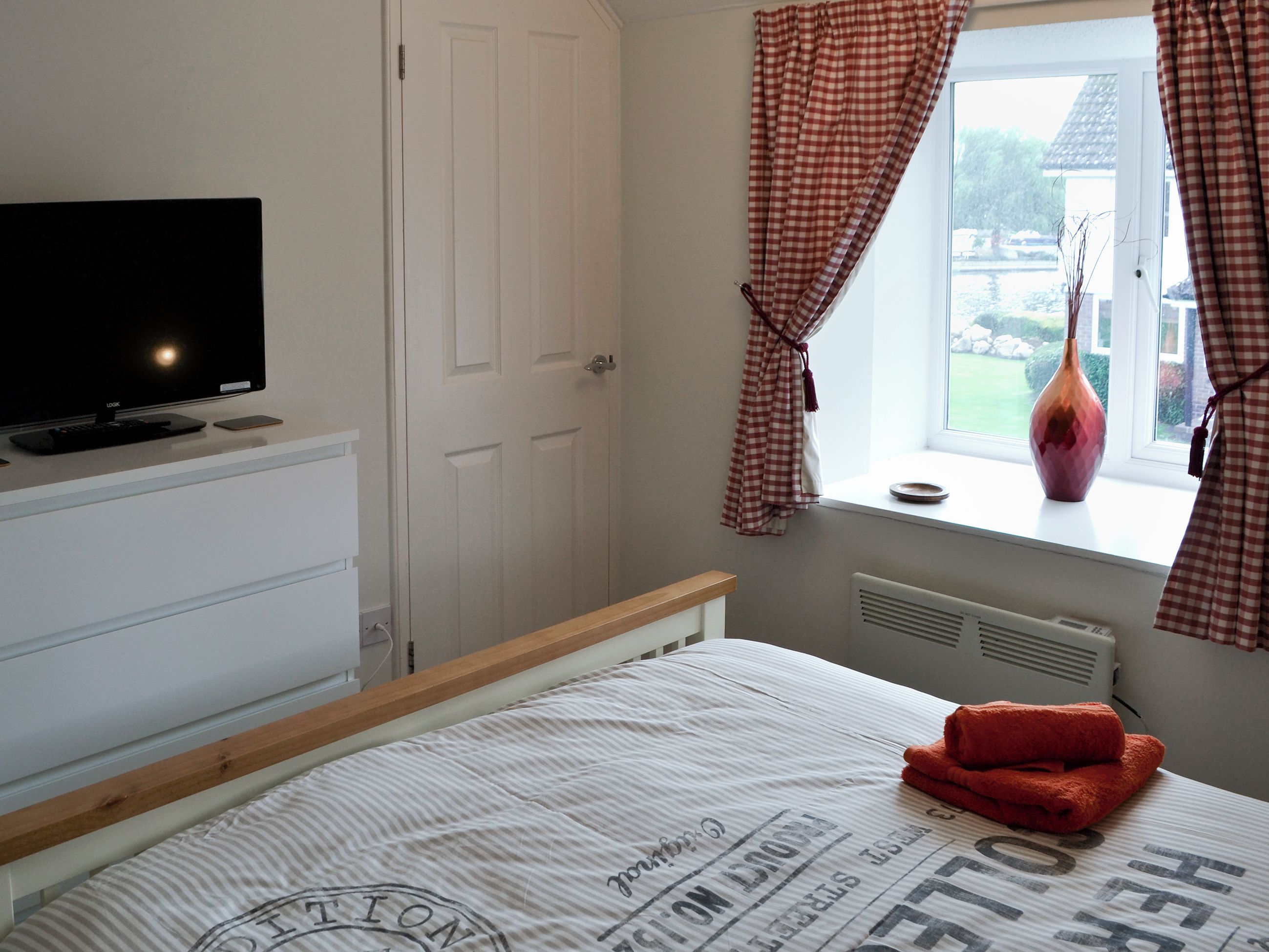 A bedroom with a bed, a TV on a stand, a window with curtains, and a radiator.