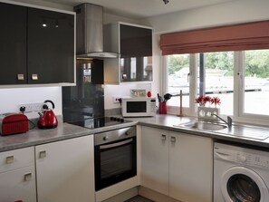 A modern kitchen with a built-in oven, microwave, and dishwasher, a kettle, and a window with a view of the outside.