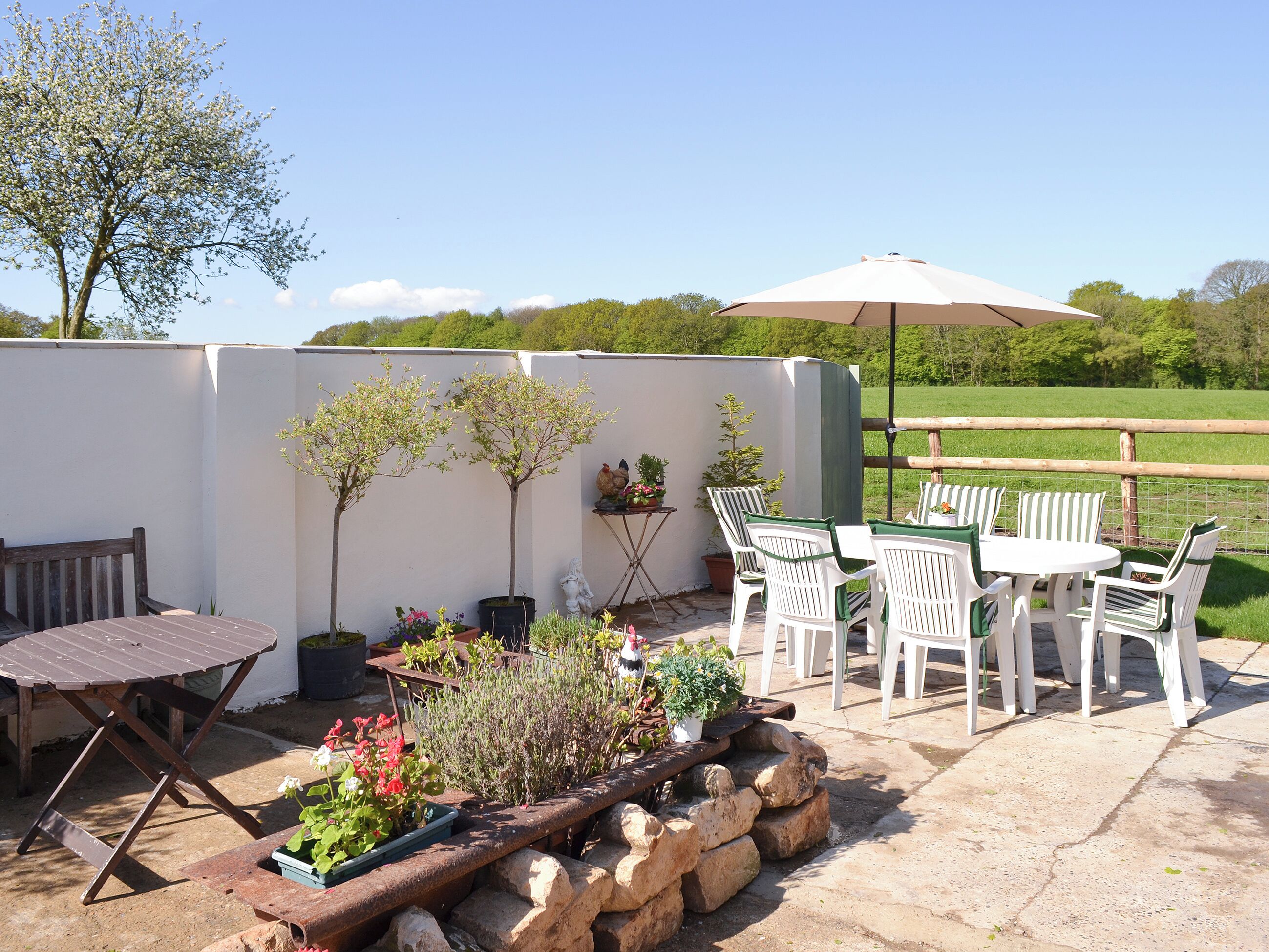 An outdoor patio with a table and chairs, surrounded by potted plants and a stone wall.