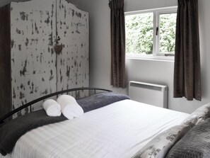 Une chambre à coucher avec un lit, une armoire, une fenêtre avec des rideaux et un radiateur.