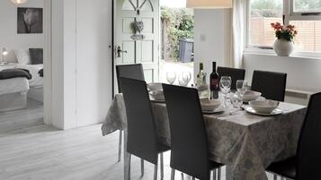 A dining area with a table set for six, chairs, a vase with flowers, and a window with a view of greenery.