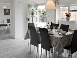 A dining area with a table set for six, chairs, a vase with flowers, and a window with a view of greenery.