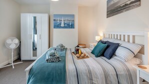 Ein Schlafzimmer mit einem Bett, einem Ventilator, einem Kleiderschrank, einem Gemälde und einem Tablett mit Frühstücksgebäck.