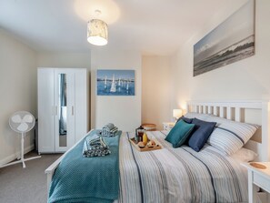 A bedroom with a bed, a fan, a wardrobe, a painting, and a tray with breakfast items.