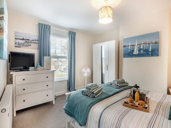 A bedroom with a bed, a TV, a dresser, a fan, and artwork on the walls.