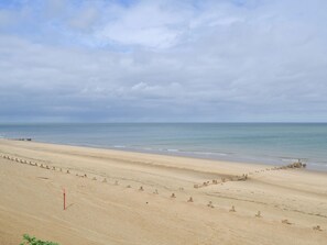 A wide sandy beach with a calm sea and overcast sky.