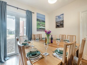 A dining area with a wooden table set for six, featuring teal and white plates, glasses, and cutlery. A vase with purple flowers is on the table. - 4 bedroom accommodation in Bacton (Bacton)