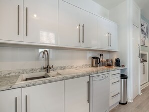 A modern kitchen with white cabinets, a marble countertop, a stainless steel sink, and a dishwasher.