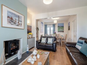 A cozy living room with a fireplace, a black leather sofa, a dining area, and artwork on the walls.